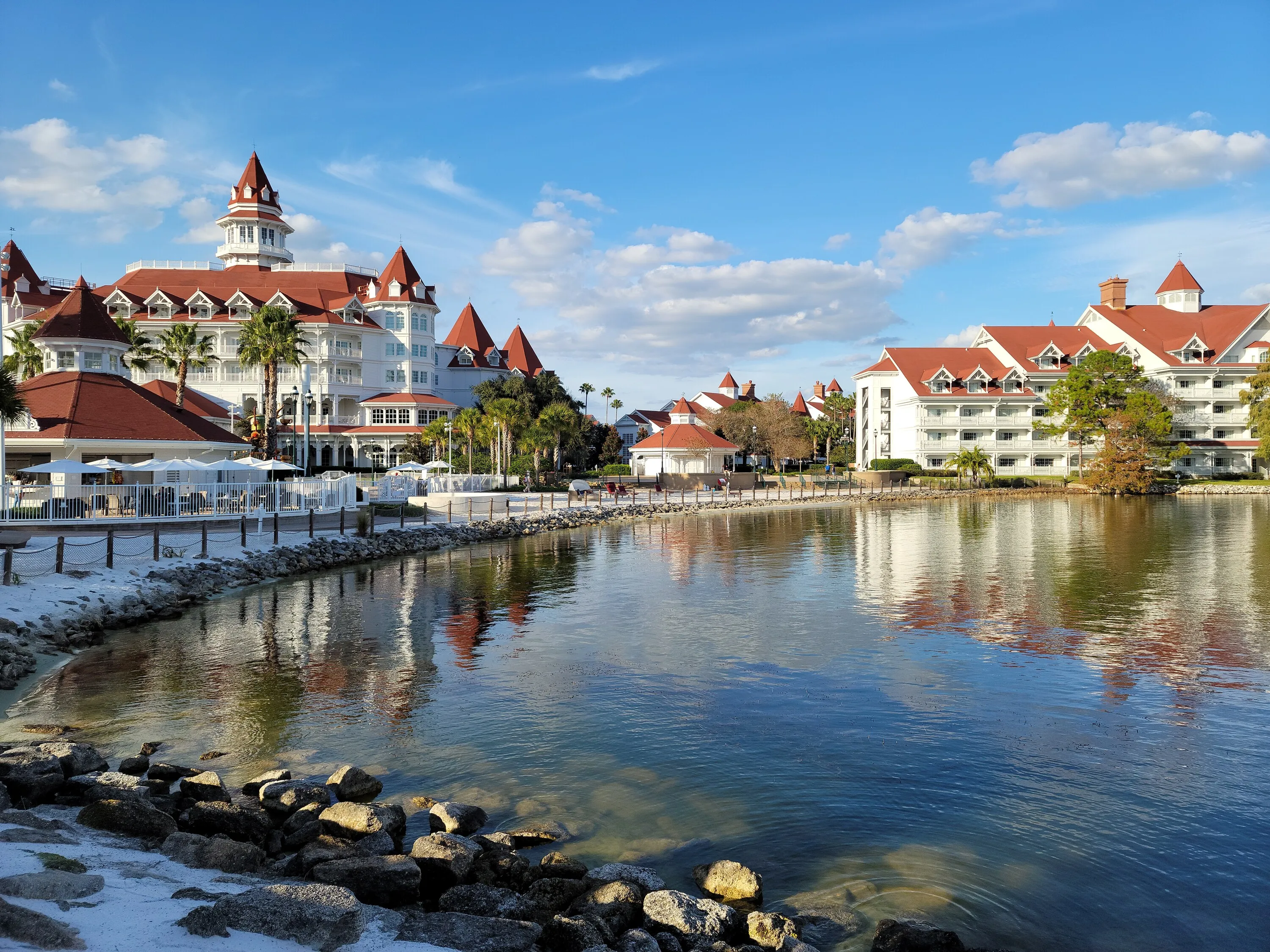 A waterfront resort with white buildings and red roofs reflected in the lagoon